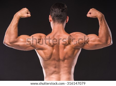 Rear view of athletic man is showing muscles of the back and hands on a dark background.