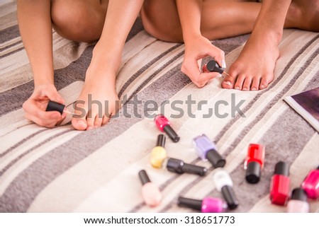 Young women are varnishing toenails on the bed at home.