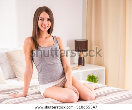 Young beautiful woman is sitting on the bed at home and smiling while looking at the camera.