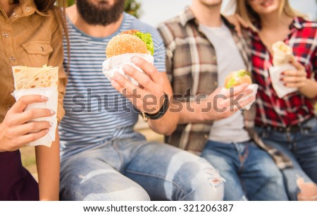 Young people walking outdoors. Sitting in the park and eat fast food