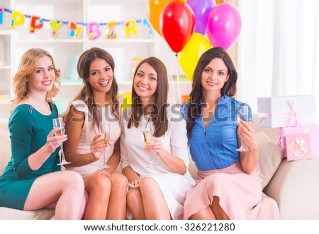 Young beautiful girls drinking champagne and smile at home party.