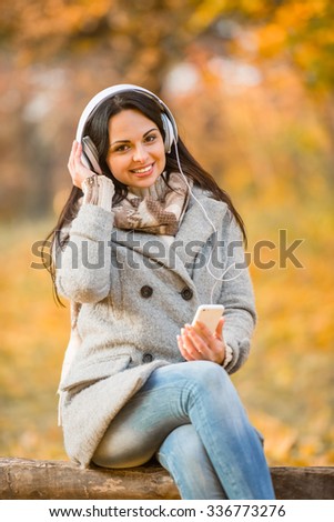 Young happy woman with headphones listening to music while walking in autumn park