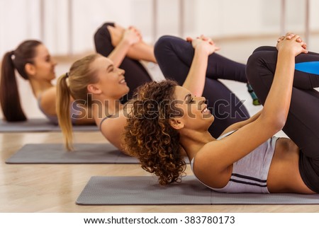 Side view of three attractive sport girls smiling while working out lying on yoga mat in fitness class