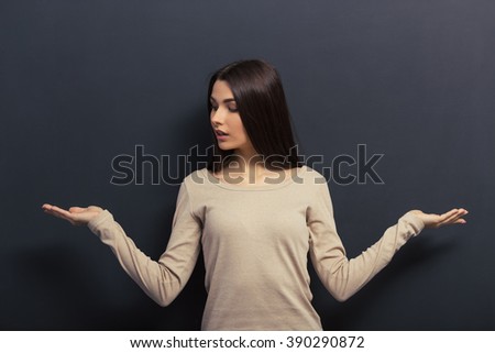 Beautiful young girl is keeping hands spread showing balance and looking to the side, standing against blackboard
