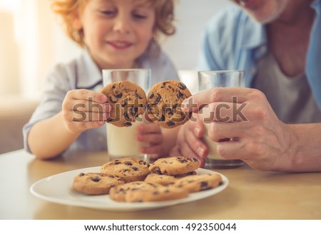 Cropped image of handsome grandpa and grandson drinking milk and eating cookies together at home