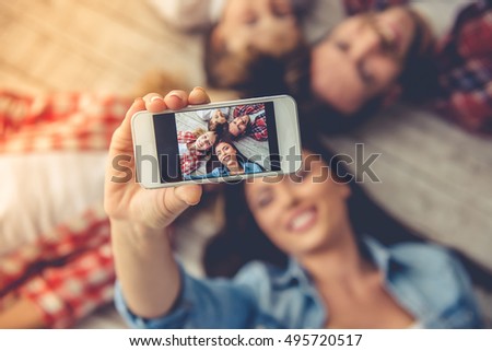 Top view of beautiful young parents and their children doing selfie using a smart phone and smiling while lying together on the floor at home