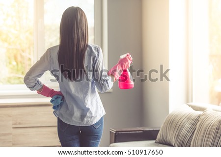 Back view of beautiful woman in protective gloves holding a spray and a rag while cleaning her house