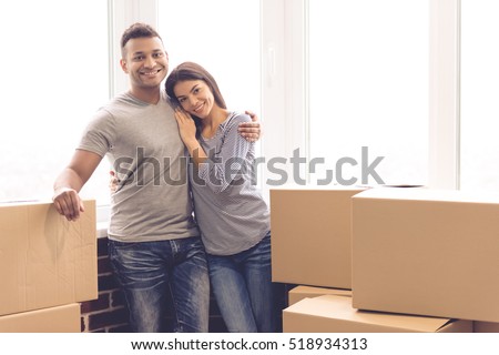 Beautiful couple is hugging, looking at camera and smiling while standing near the boxes ready to move