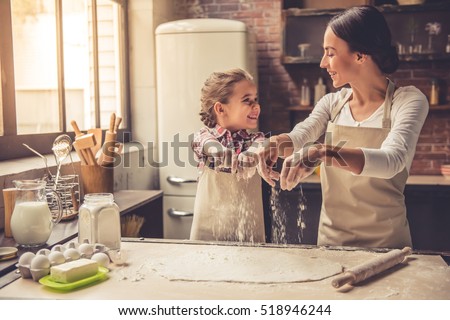 Cute little girl and her beautiful mother are sprinkling the dough with flour and smiling while baking