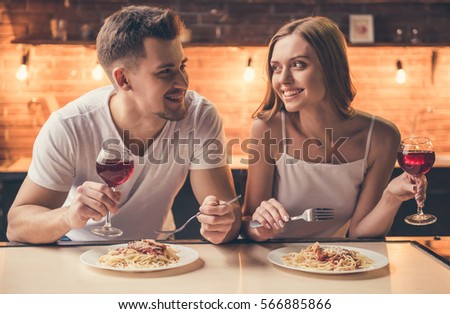 Beautiful couple is talking and smiling while having a romantic dinner together in the kitchen