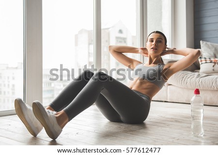 Attractive slim girl in sportswear is doing abs exercises on the floor at home