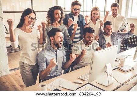 Successful young business people are raising hands in fists and screaming with happiness while working with a computer in business center