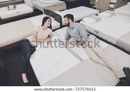 A man in a gray shirt and a woman in a light T-shirt lay on a mattress in the store. They\'re going to buy a mattress. They lie on it and look at each other