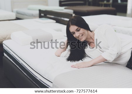 A woman in a white shirt and jeans in a mattress store. She examines the mattress she wants to buy. She lay down on the mattress and examines it.