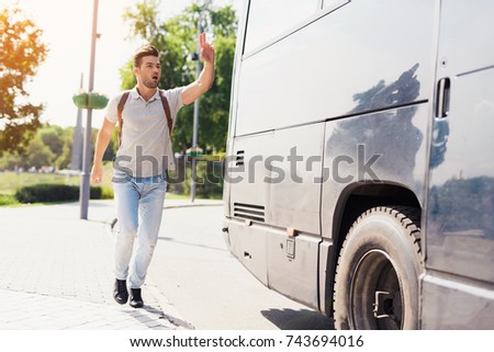 The guy runs after the bus that leaves. He missed the bus and tries to catch up with him. He runs after a modern black bus and waves his hand to stop it.