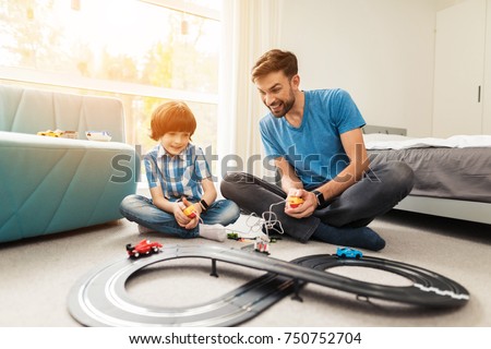 Father and son compete in races with children\'s cars. They play together on the floor in their house. This is a children\'s toy.