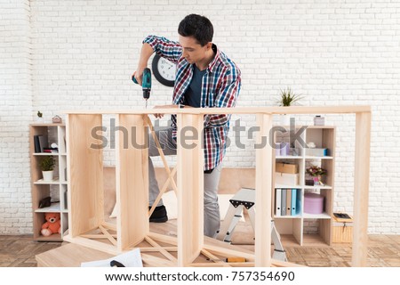 The young man tries himself to fold his bookcase. He uses tools for furniture. He will use this furniture for the interior of his room.