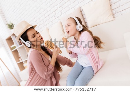Mom and daughter sing songs at home. They use combs like microphones. They play together.