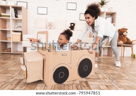 Mom and daughter are playing with big toy cars. They are at home. African American girl and a woman.