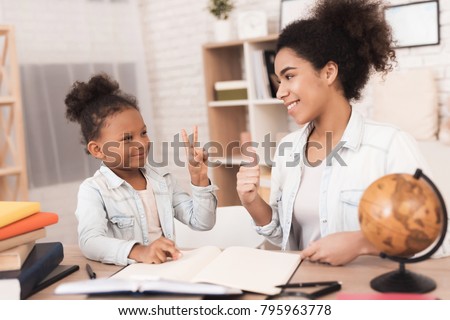 Mom and daughter together do their homework in school. They are both mulattoes. Mom helps a little girl learn.