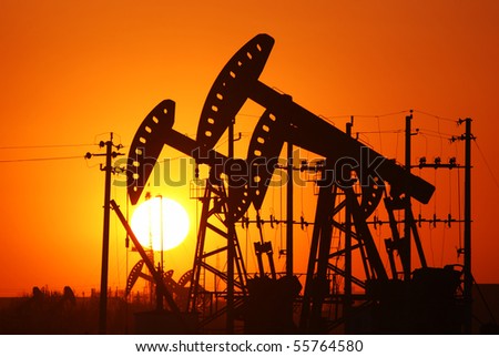 An oil pump jack is silhouetted by the setting sun