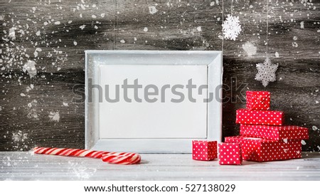 White photo frame with christmas decoration on the wooden table. Red boxes and snowflakes on the grey background. New year greeting card template. Holiday mock up. Scandinavian style.