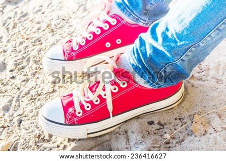 Feet concept with red shoes on sand background.