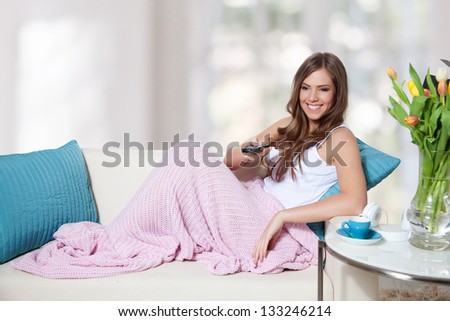 Beautiful young woman changing TV channel with remote control