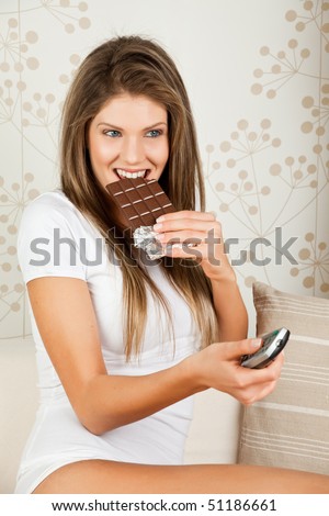 beauty young woman eating chocolate and holding a remote control