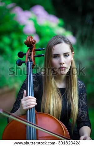 Pretty blonde girl in black dress playing a cello in a rural outdoor
