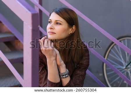 Young joyful tan woman sitting on bright stairs of urban building with bicycle
