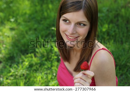 Smiling pregnant young woman sitting on green grass with basket of juicy strawberry in hands