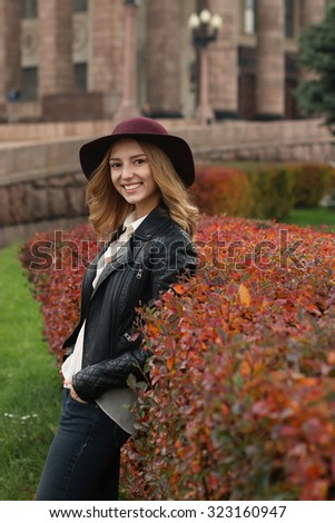 Autumn in the city.Smiling blonde woman in hat in front of urban background.