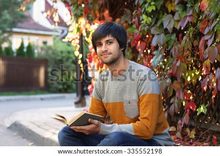 Young handsome man with old book in his hands on autumn background