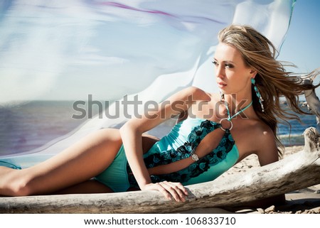 Young woman in bikini posing near a snag on a beach