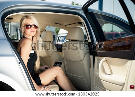 Young blond lady sitting on a backseat of a luxury car - stock photo