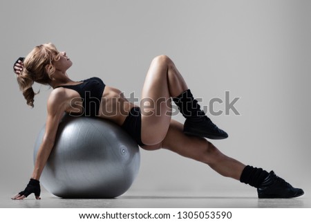 Athletic woman lies on a gym ball on gray background