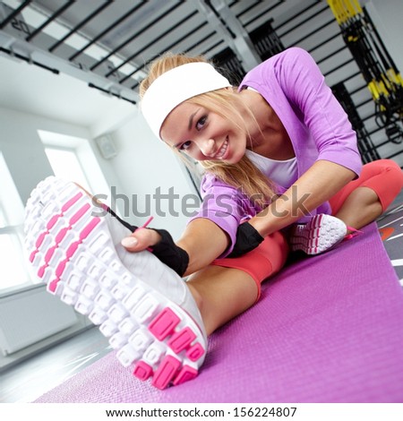 Smiling athletic woman stretches the muscles in a gym