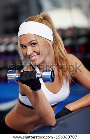 Smiling athletic woman pumping up biceps in a gym