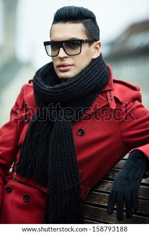 Fashionable male model posing outdoors in red coat and black scarf