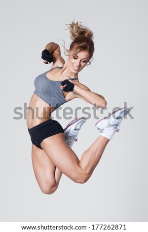 Young woman jumps while making aerobics exercises on gray background