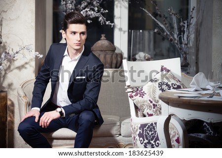 Handsome young man in a classic suit sitting on a sofa in restaurant