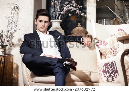 Handsome young man in a classic suit sitting on a sofa in restaurant