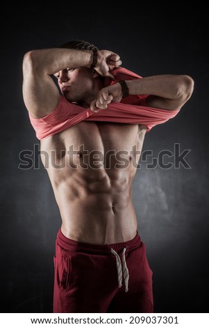 Brutal athletic man taking shirt off on dark background