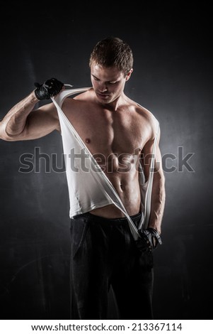 Brutal athletic man rips shirt on dark background