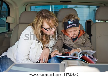 mother and her son are reading a book on a backseat of a car
