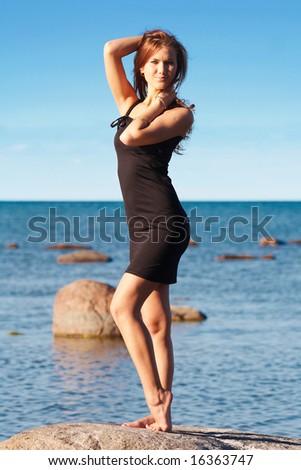 Young lady in black dress near the sea touching her hair