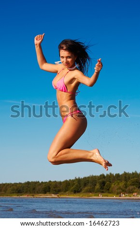 Woman in pink bikini jumps high on a beach