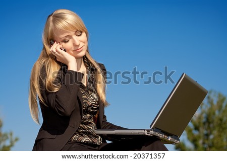 Young blonde business woman working on laptop computer and talking on cell phone