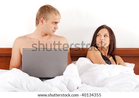 Man with laptop lying in bed and woman is angry